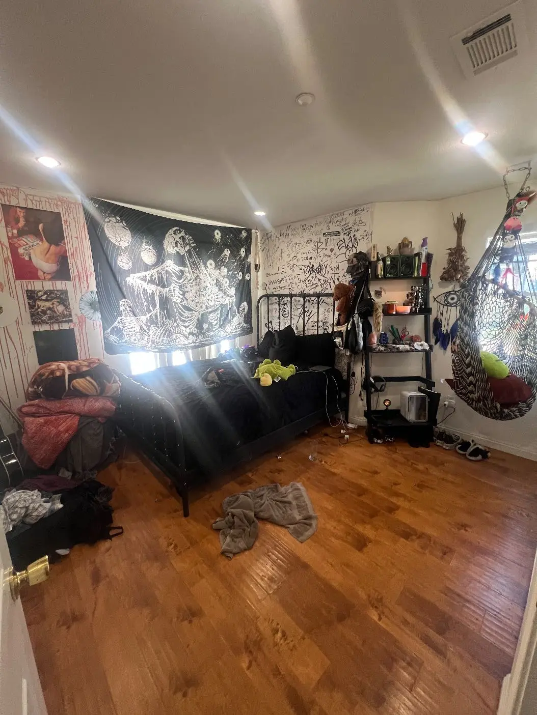 <p>Create an image of a medium-sized bedroom (around 12x14 feet) that is a fusion of punk, goth, and hippie design styles. The room should predominantly feature black and white colors, with occasional pops of color for a blend of calmness and vibrant aesthetics. Include modern and adjustable lighting solutions to cater to various mood settings. The furniture should take a minimalist stance, with multi-purpose pieces like a bed that doubles as storage, organized shelves, and an aesthetic hammock. The floor should be of a dark wood or polished concrete material, adding to the overall edgy atmosphere.</p>