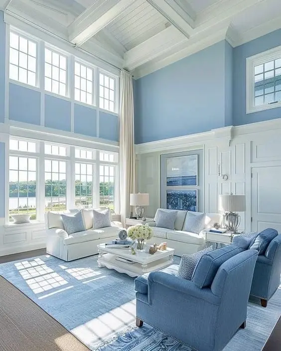 <p>Visualize a spacious living room of approximately 20 x 15 feet, embellished with high ceilings reaching 18 feet, adorned with white wooden beams. The room is decorated with light blue walls and wainscoting, enhancing the minimalist coastal design. There are large windows that open up to a picturesque landscape, draped with elegant curtains. The furniture layout consists of two plush white sofas and two blue armchairs centered around a chic white coffee table. The room features wooden flooring, and is graced by organic elements such as indoor plants and a textured rug, infusing a warm and inviting atmosphere.</p>