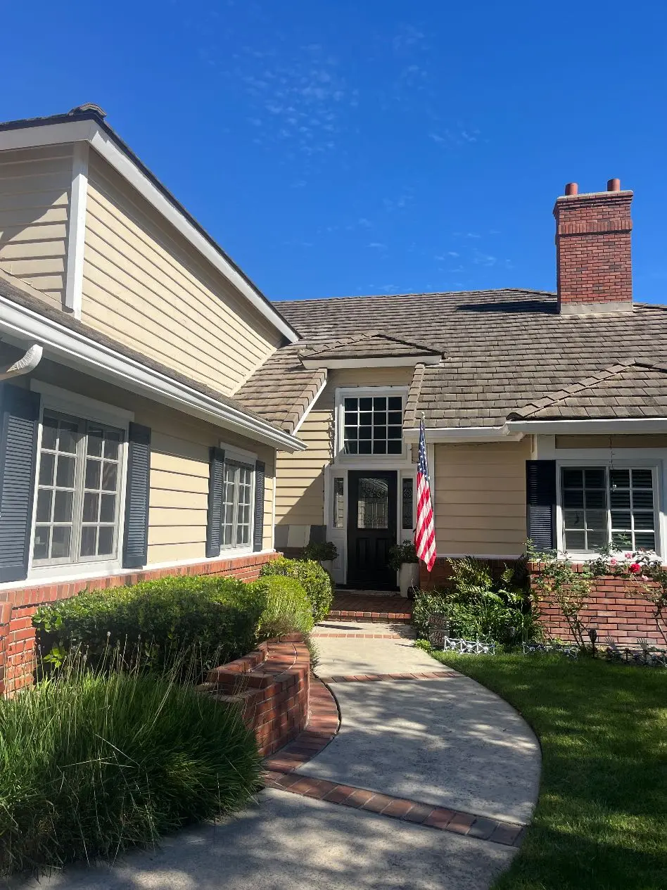 <p>A vivid image of a skillfully remodeled exterior entrance of a house, unfolding over an approximate area of 300 square feet. The pathway is broadened to a six feet width, lined with inviting natural stone tiles. The garden is orderliness personified and replete with symmetrical arrangements of low-maintenance plants interspersed with vibrant blooming flowers. The conventional brick borders give way to stone planters, forging soft boundaries in this serene space. Strategically placed lights lend an inviting glow as dusk sets in. The exterior walls flaunt a fresh coat of modern paint, its soft earthy tones blending in perfectly with the surroundings. Enhanced with new materials, the roof and chimney sport a polished, pristine look.</p>